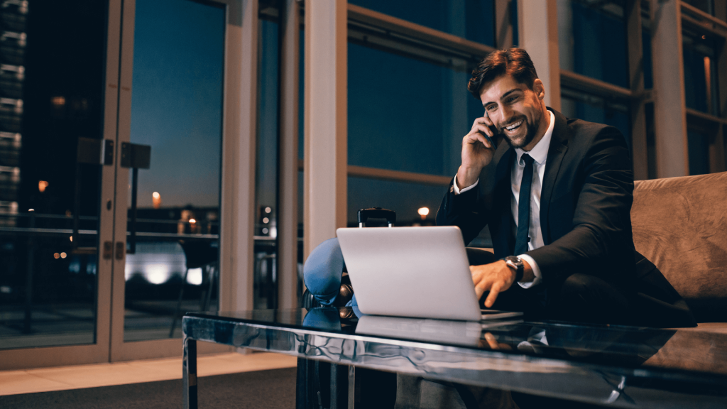 a businessman works on a laptop computer and talks on the phone at an airport