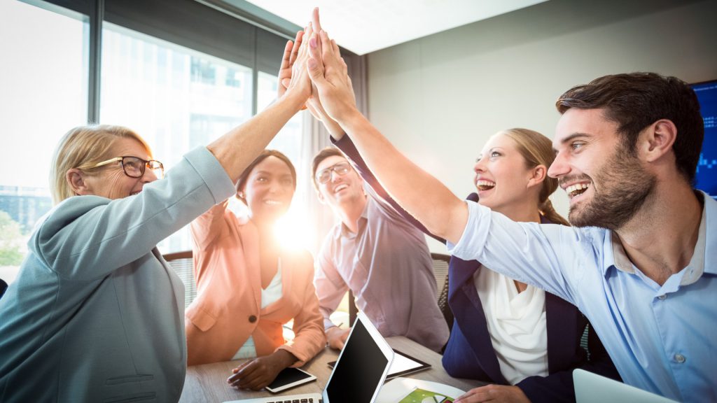 a team of people high fives over a laptop computer