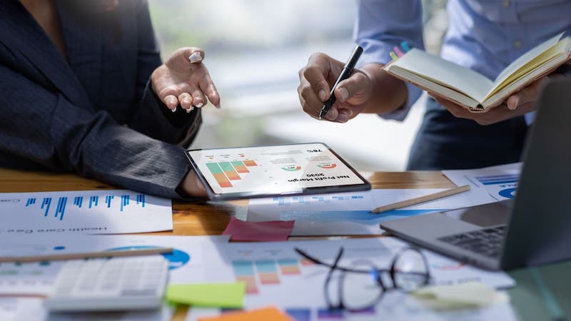 Close up of manager reviewing profit margin report over a cluttered desk | Organizing customer data in a CRM