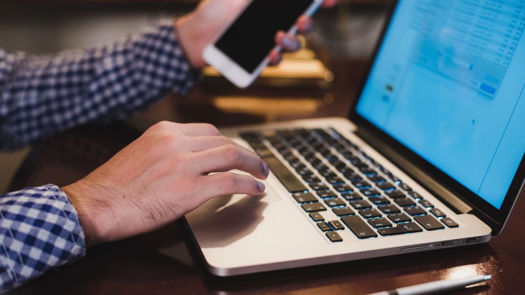 Close Up of Salesperson Typing on Laptop Keyboard and Holding Smartphone | What is CRM Integration?