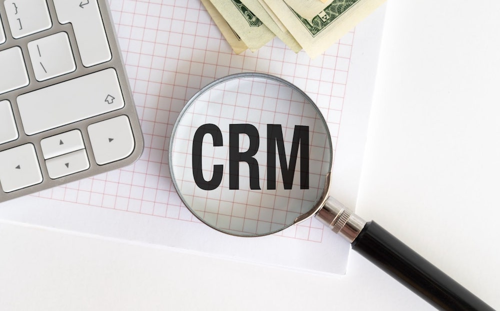 Magnifying glass over the acronym, “CRM” | CRM ROI